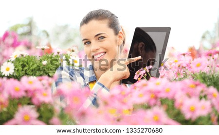 smiling woman in garden of flowers daisies touch screen of digital tablet, spring concept and internet search