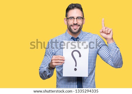 Handsome young business man holding paper with question mark over isolated background surprised with an idea or question pointing finger with happy face, number one
