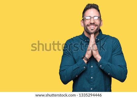 Young handsome business man wearing glasses over isolated background praying with hands together asking for forgiveness smiling confident.