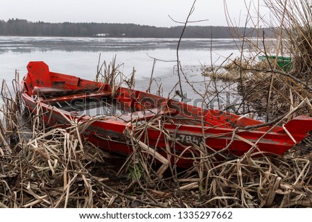 Old wooden red fishing boat on the lake. Monochrome winter lanscape and ice on the water. Frozen water in the boat. Atmospheric picture. 