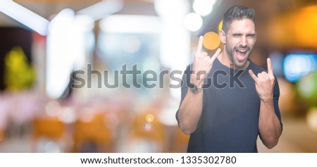 Young handsome man wearing sweater over isolated background shouting with crazy expression doing rock symbol with hands up. Music star. Heavy concept.