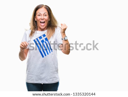 Middle age hispanic woman holding flag of Greece over isolated background screaming proud and celebrating victory and success very excited, cheering emotion