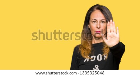 Beautiful middle age woman wearing rock and roll sweater doing stop sing with palm of the hand. Warning expression with negative and serious gesture on the face.