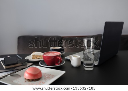 Open laptop, cups of coffee, dessert, stationery on black background. Freelancer work concept. Space for text.
