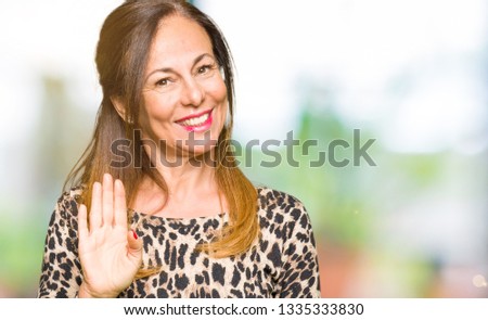 Beautiful middle age woman wearing leopard animal print dress Waiving saying hello happy and smiling, friendly welcome gesture