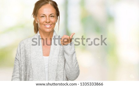 Beautiful middle age adult woman wearing winter sweater over isolated background doing happy thumbs up gesture with hand. Approving expression looking at the camera with showing success.