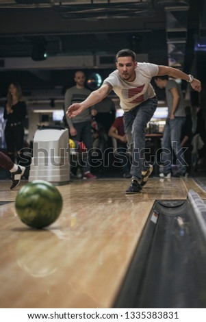 Friends enjoying bowling at club. Young man at night bowling throwing ball in a bowling alley