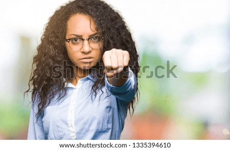 Young beautiful business girl with curly hair wearing glasses Punching fist to fight, aggressive and angry attack, threat and violence