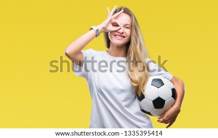 Young beautiful blonde woman holding soccer ball over isolated background with happy face smiling doing ok sign with hand on eye looking through fingers