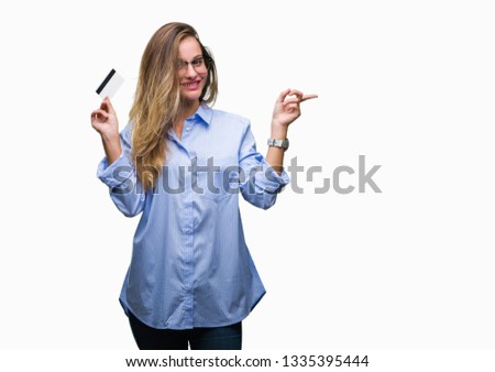 Young beautiful blonde woman holding credit card over isolated background very happy pointing with hand and finger to the side