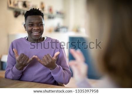 Teenage Boy And Girl Having Conversation Using Sign Language Royalty-Free Stock Photo #1335397958