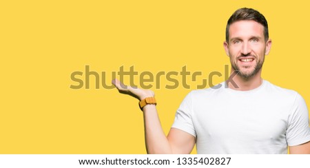 Handsome man wearing casual white t-shirt smiling cheerful presenting and pointing with palm of hand looking at the camera.