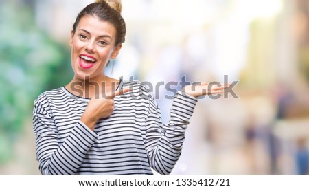 Young beautiful woman casual stripes sweater over isolated background amazed and smiling to the camera while presenting with hand and pointing with finger.