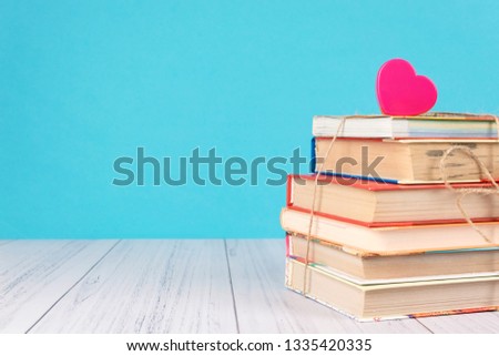 Stack of books and pink heart. Books with jute ribbon bow as gift on blue background. Education background with copy space, back to school concept.