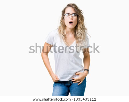 Beautiful young blonde woman wearing glasses over isolated background In shock face, looking skeptical and sarcastic, surprised with open mouth