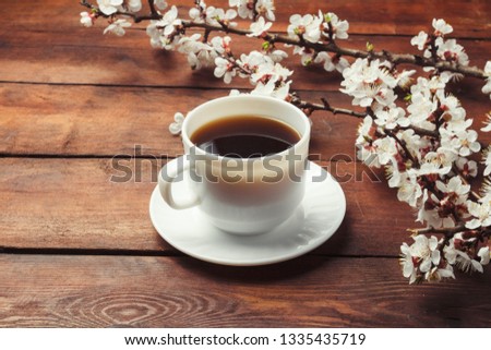 Sakura branches with flowers and a white cup with a black coffee on a dark wooden background. Concept of Spring