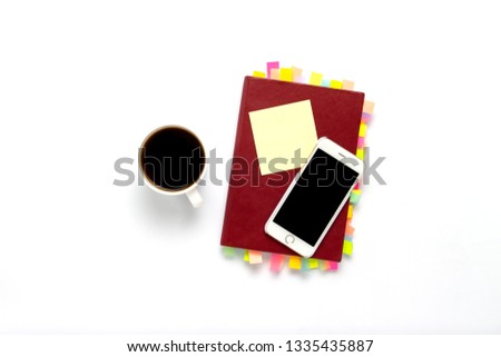 Red diary with stickers on the pages, a cup with black coffee, telephone, white background. Concept of a successful business, a lot of meetings and plans for a long period. Flat lay, top view