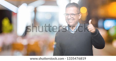 Middle age bussines arab man wearing glasses over isolated background doing happy thumbs up gesture with hand. Approving expression looking at the camera with showing success.