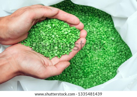 A hands hold or touching biodegradable plastic pellets, plastic polymer dye granules color clear green Royalty-Free Stock Photo #1335481439
