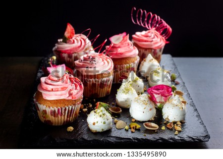 Pink cream cupcakes decorated with strawberries and meringues sprinkled with nuts, decorated with flowers.