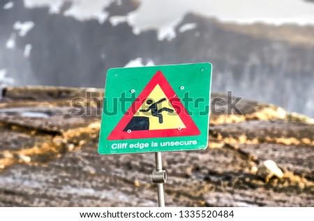 Warning sign at the edge of a ravine in Iceland,  supported by a graphic illustration, indicating the cliff edge is unsafe