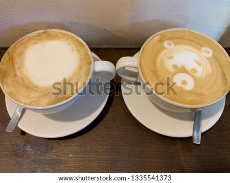 Two white cups with cappuccino, coffee with milk foam and picture of bear face closeup