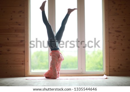 The girl is engaged in yoga on the rug in front of the window
