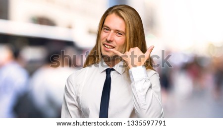 Blond businessman with long hair making phone gesture. Call me back sign at outdoors