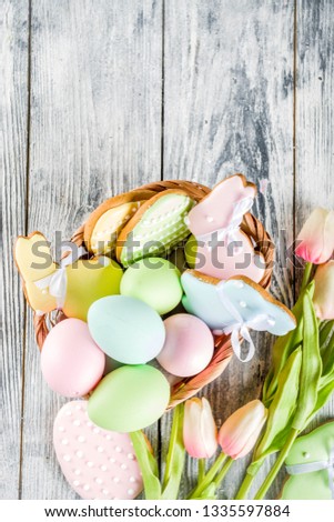 Easter greeting card background with pastel colored eggs and homemade cookies shaped in eggs and bunnies rabbits. With a basket, tulips, rustic wooden table, copy space top view banner