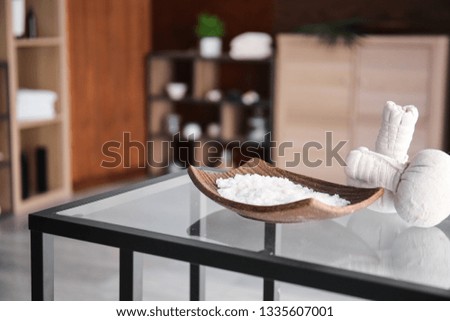 Plate with sea salt and herbal bags on table in spa salon
