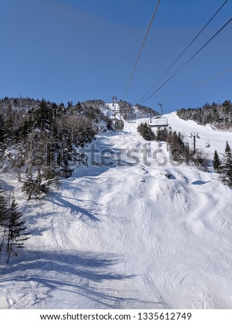 Ski chair lifts and gondolas going up over ski trails. 
Mont Orford, Magog, Quebec, Canada.