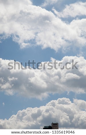 Textures in a sunny cloudy blue sky with a building top in the bottom, kind of like a Magritte painting Royalty-Free Stock Photo #1335619046