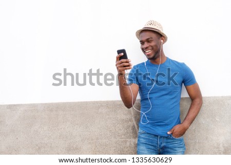 Portrait of happy young black man listening to music with mobile phone and earphones