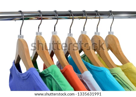 T-shirts of different colors hang on closing rack on wooden hangers with plastic size tags indexes of the XXS, XS, S, M, L, XL, XXL are isolated on white background.