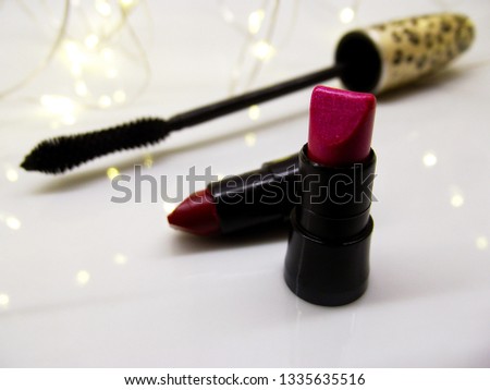Close up photo about two mini lipstick samples and a black mascara. A micro led light garland is in the background.