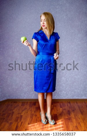A woman in a blue dress on a purple background holding a green apple and smiling