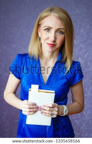 A woman in a blue dress on a purple background holding a white notebook