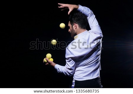 Stylish Man in white shirt posing for the camera. Man juggling yellow balls on black background.