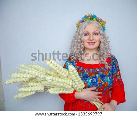 cute plump girl from the village in a red summer sundress with a sheaf of wheat in her hands on white studio solid background