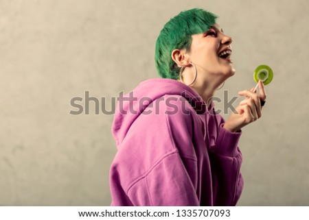 Sweets lover. Delighted green haired woman smiling while holding a sweet lollipop