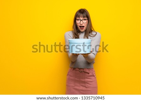 Woman with glasses over yellow wall surprised because has been given a gift