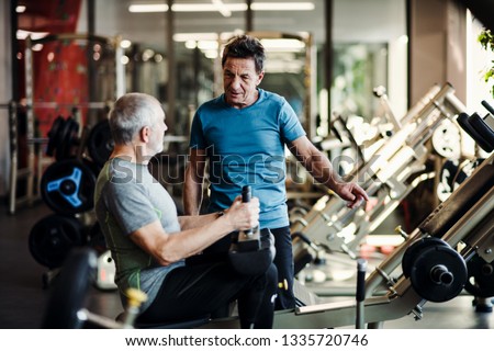 A senior man with a young trainer doing strength workout exercise in gym.