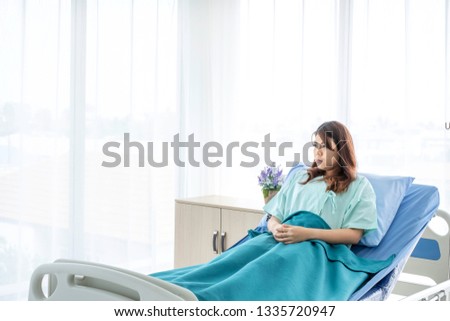 Portrait of sad female patient in uniform in hospital bed with unhappy expression. The sick inpatient worry about medical expenses as she recovering from flu. Insurance concept. Copy space given. 