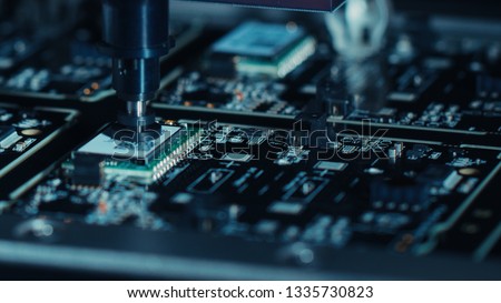 Close-up Macro Shot of Electronic Factory Machine at Work: Printed Circuit Board Being Assembled with Automated Robotic Arm, Place Technology Mounts Microchips to the Motherboard Royalty-Free Stock Photo #1335730823