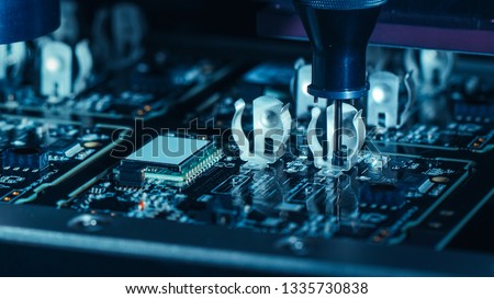 Close-up Macro Shot of Electronic Factory Machine at Work: Printed Circuit Board Being Assembled with Automated Robotic Arm, Pick and Place Technology Mounts Microchips to the Motherboard. Royalty-Free Stock Photo #1335730838
