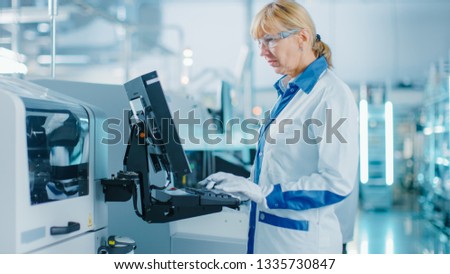On High Tech Factory Female Engineer Uses Green Screen Computer for Programing Pick and Place Electronic Machinery for Printed Circuit Board Surface Mount Assembly Line.