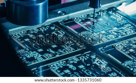 Factory Machinery at Work: Printed Circuit Board Being Assembled with Automated Robotic Arm, Pick and Place Technology Mounts Microchips to the Motherboard. Macro Close-up. Royalty-Free Stock Photo #1335731060