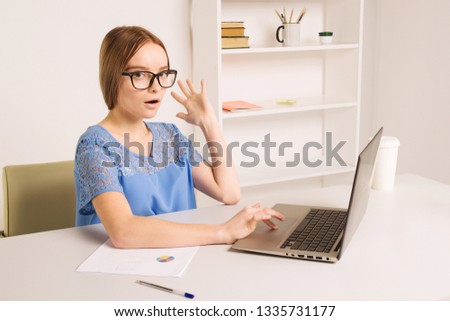 Portrait of an attractive woman at the table with cup and laptop, book, notebook on it, grabbing her head. Bookshelf at the background, concept photo - Image