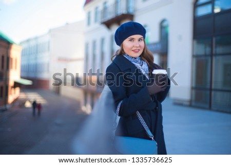 girl in a coat with coffee walks through the city