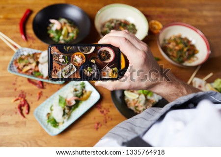 Top view closeup of unrecognizable man taking picture of Asian food dishes, copy space